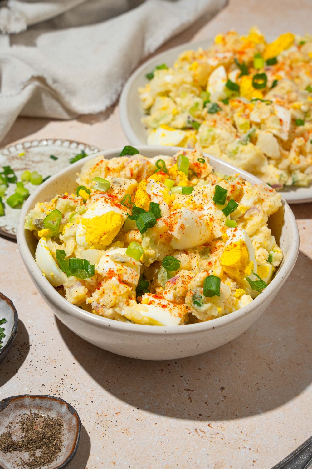 A white bowl with deviled egg potato salad garnished with sliced green egg and paprika. The bowl is on a tan counter with an additional plate of potato salad.