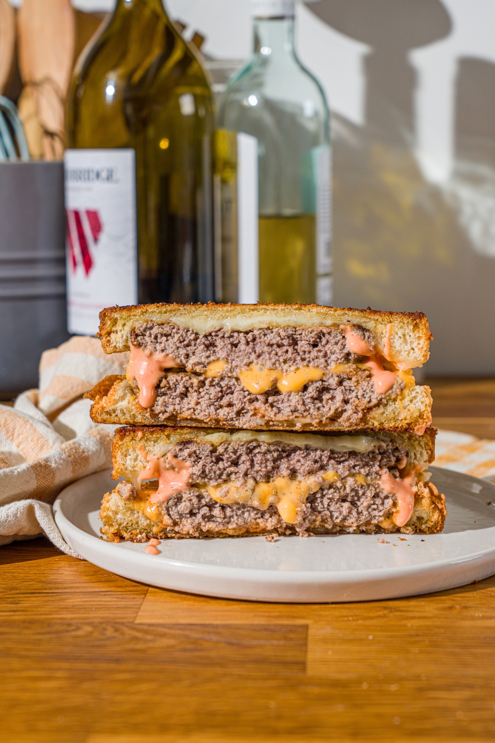 A white plate with a frisco melt with frisco sauce sliced in half and stacked on top of one another. The plate is on a wooden counter with a white cloth napkin.