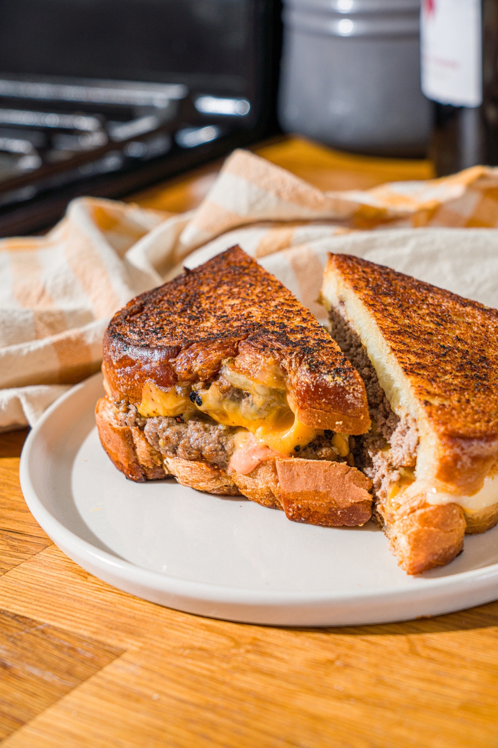 A white plate with a frisco melt with frisco sauce sliced in half. The plate is on a wooden counter with a white striped napkin.