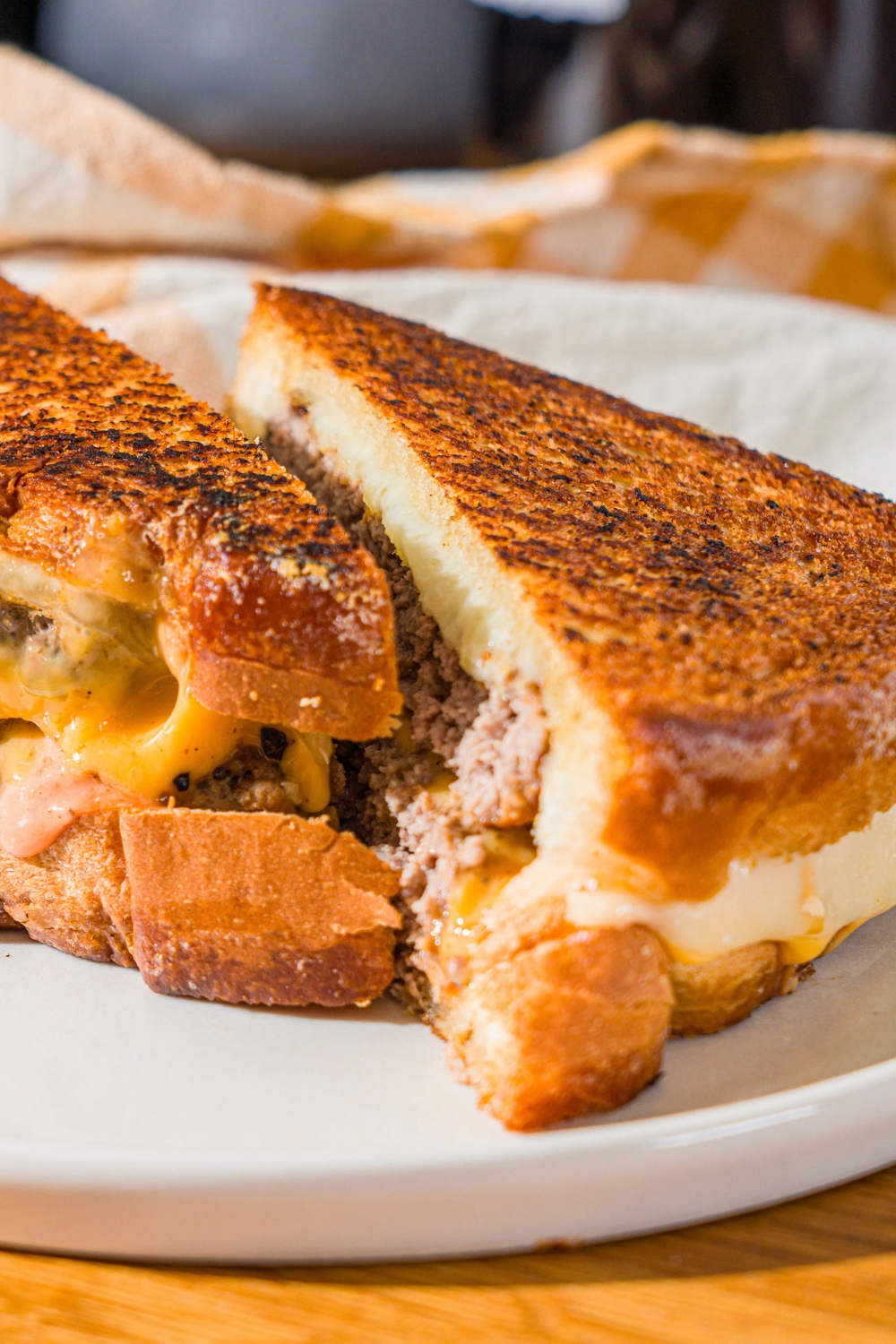A white plate with a frisco melt with frisco sauce sliced in half. The plate is on a wooden counter with a white striped napkin.