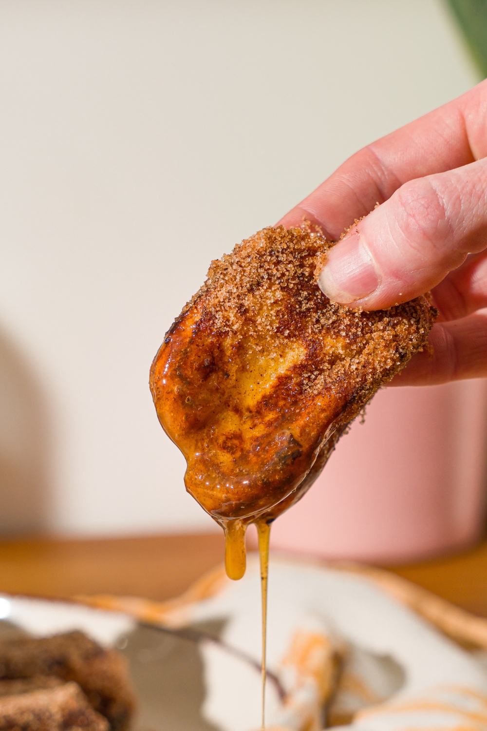 A hand holding a Hawaiian french toast bite dipped in caramel dipping sauce.