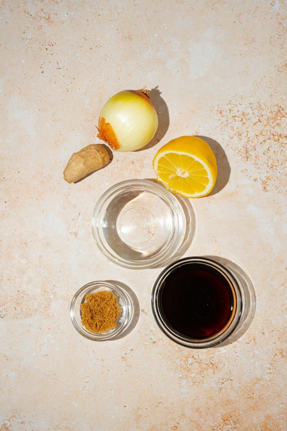 A tan counter with ingredients to make hibachi ginger sauce including ginger, tamari, rice vinegar, brown sugar, lemon, and yellow onion.