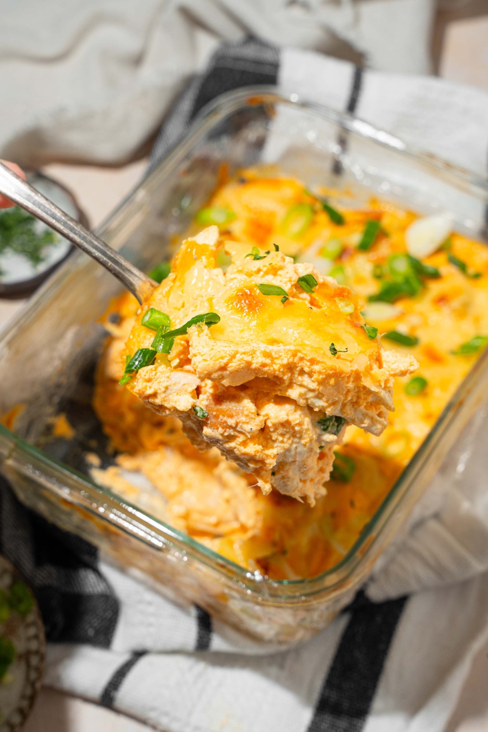 A close up of a spoon with a bite of cottage cheese Buffalo chicken dip with a baking dish of dip blurred in the background.