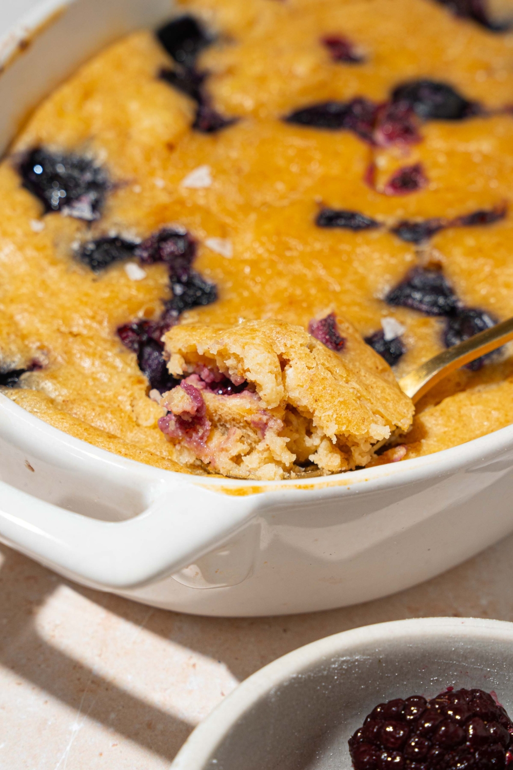 A baked protein pancake bowl with blueberries. There is a spoon taking a bite from the bowl.
