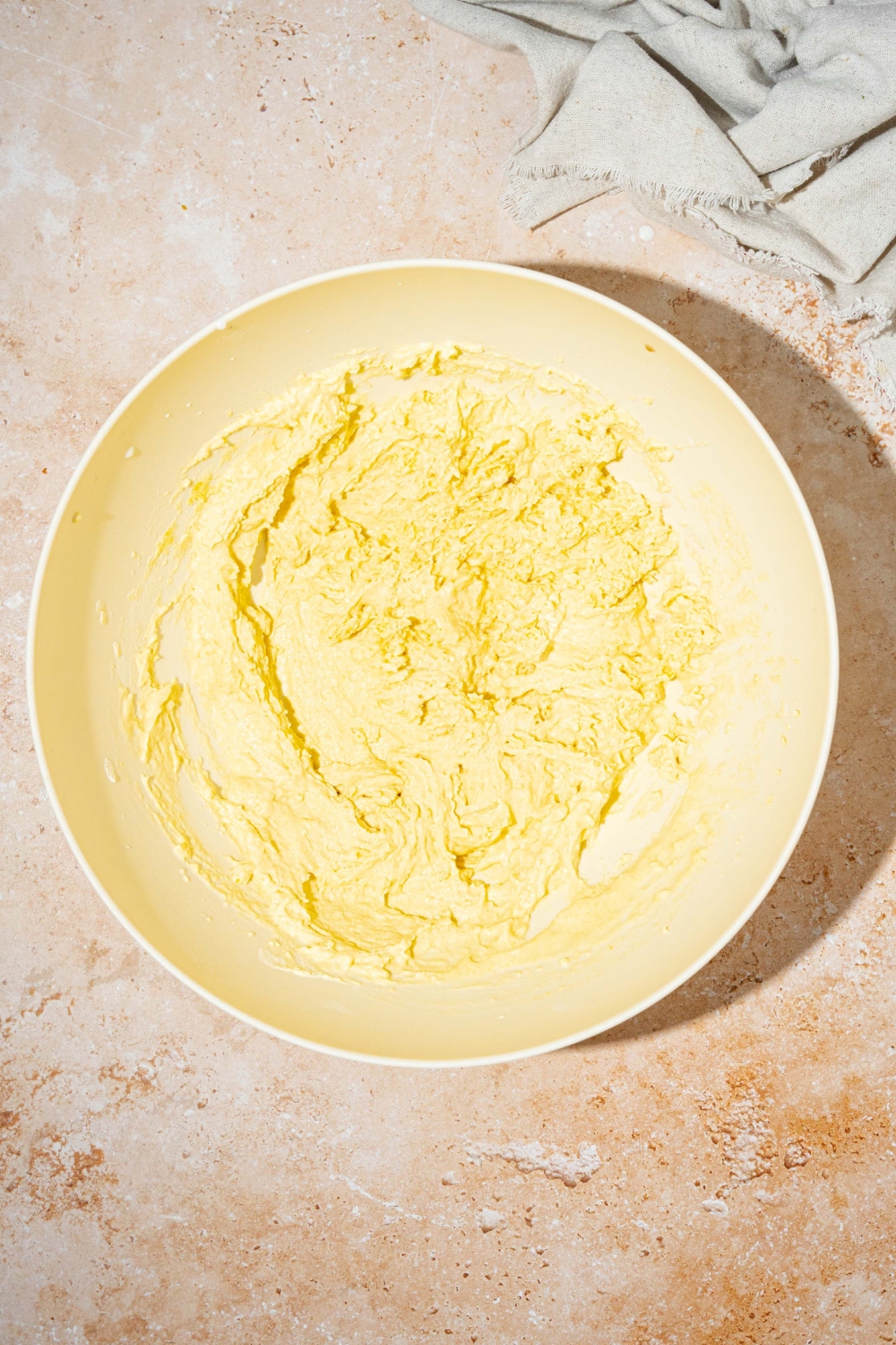 A large white bowl with cornbread dough made without eggs. The bowl is on a tan counter.