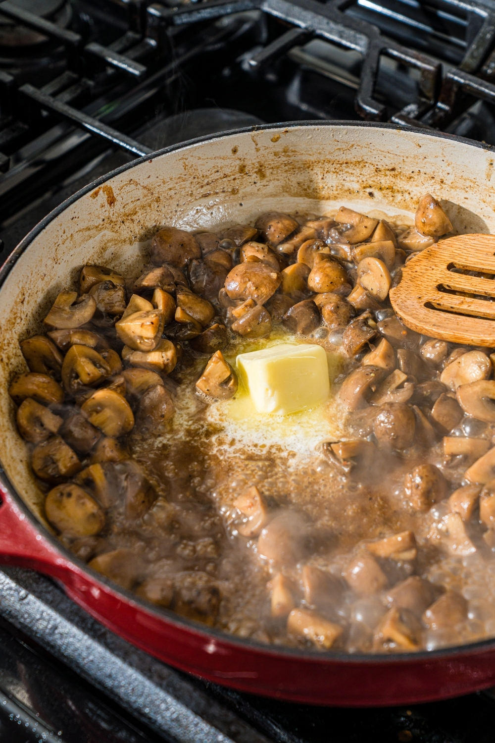 A cast iron skillet with roasted mushrooms cooking in butter. The skillet is on a stove.