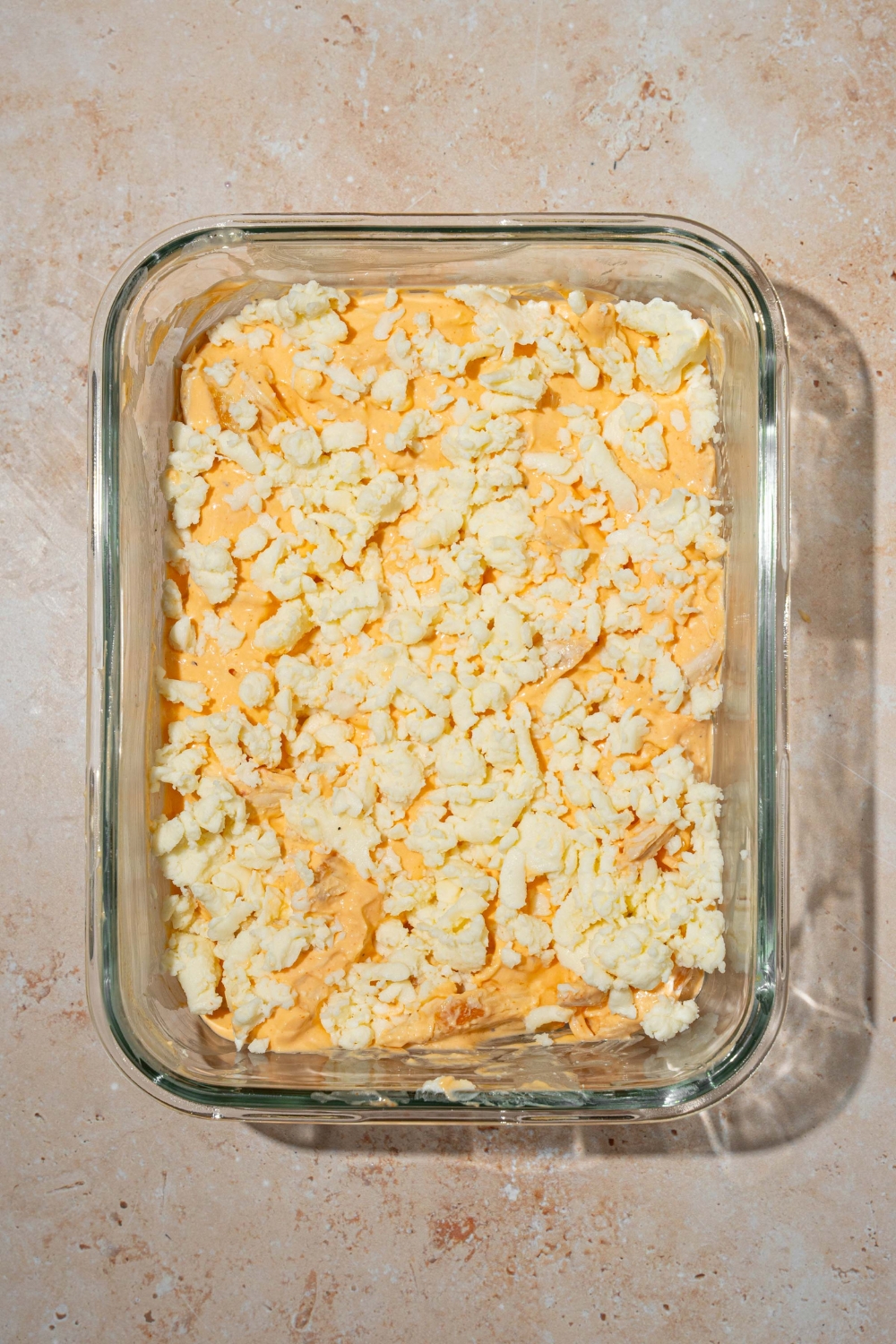 A glass baking dish with cottage cheese Buffalo chicken mixture topped with shredded cheese. The dish is on a tan counter.