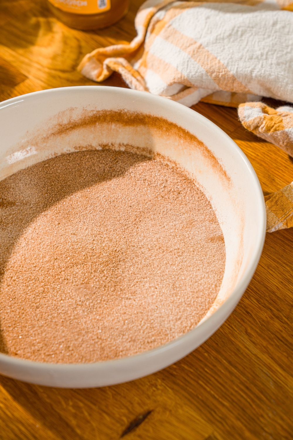 A large white bowl with a cinnamon sugar mixture. The bowl is on a wooden counter with a yellow striped napkin.