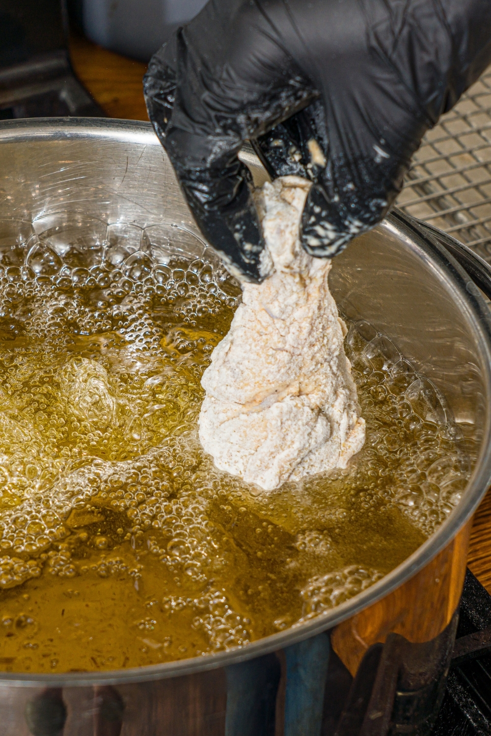 A hand placing a piece of chicken coated in seasoned flour into a pot of frying oil.