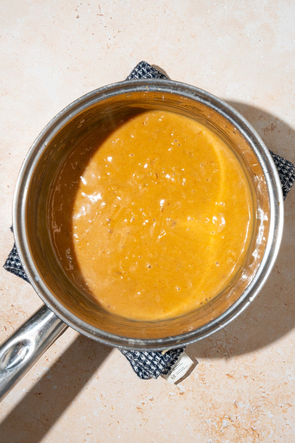 A pot with cooked peanut sauce. The pot is on a tan counter with a dish sauce.