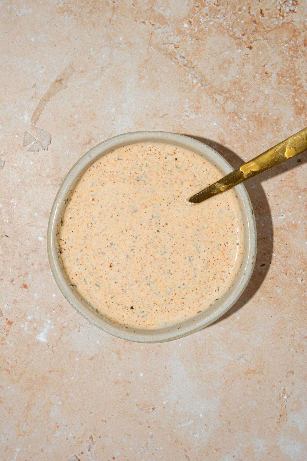 A white bowl with Popeyes blackened ranch. A spoon is in the bowl. The bowl is on at tan counter.