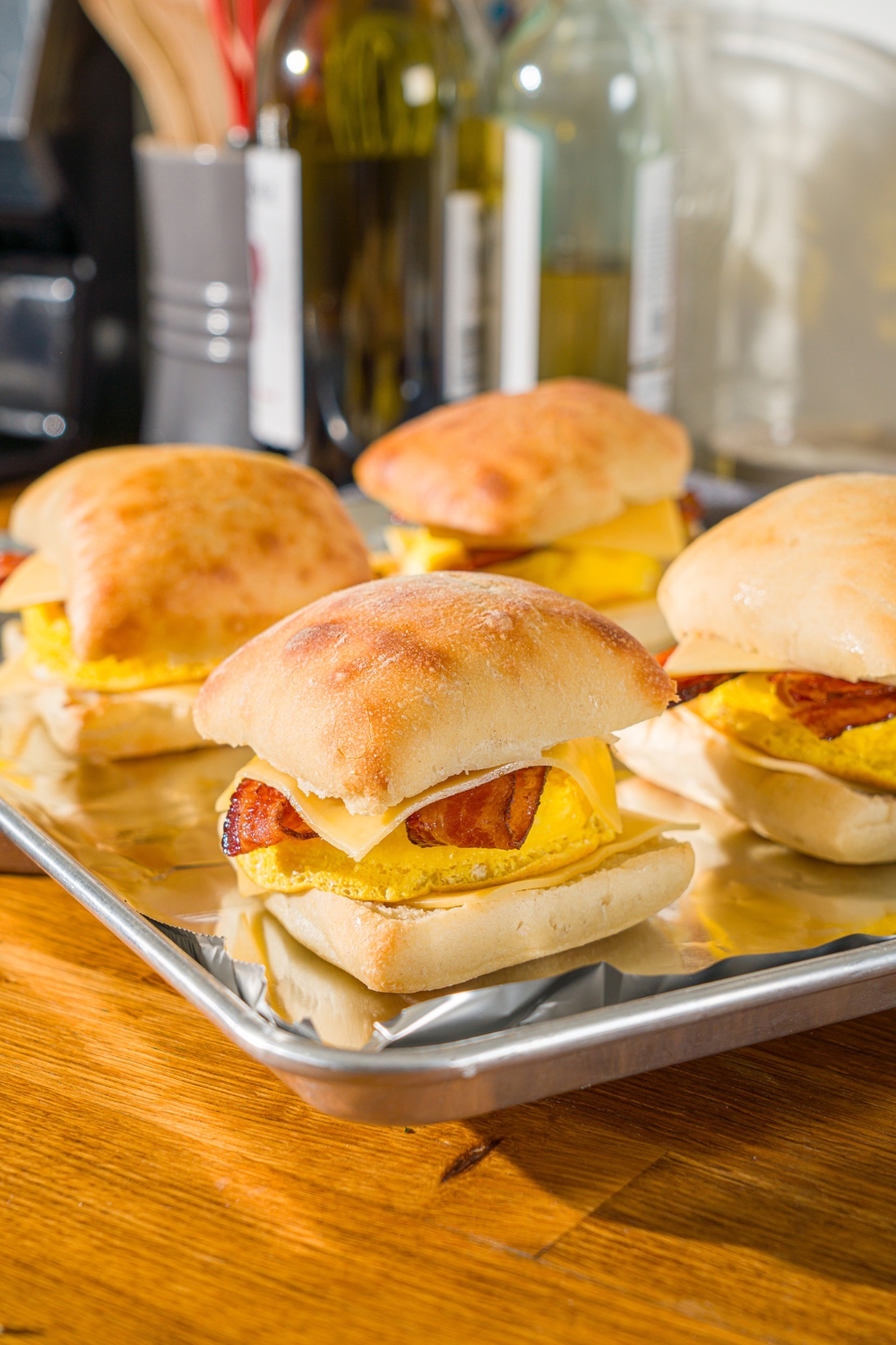 A baking sheet lined with foil with several unbaked Starbucks gouda bacon egg sandwiches. The sheet is on a wooden counter.