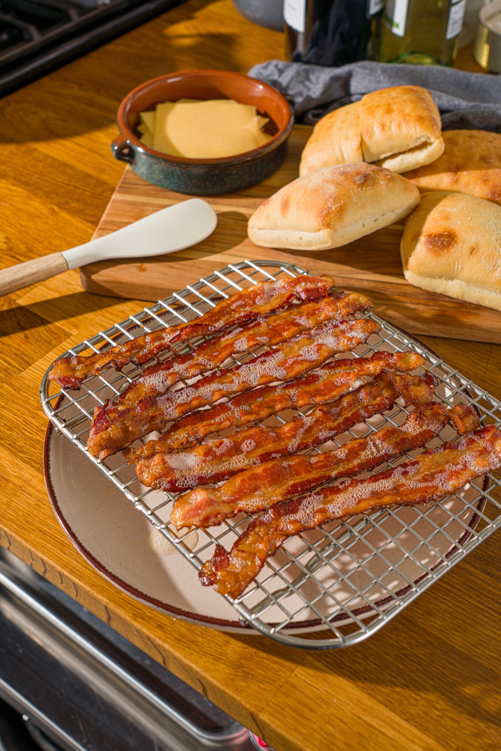 A drying rack over a white plate with several pieces of cooked bacon. The plate is on a wooden counter.