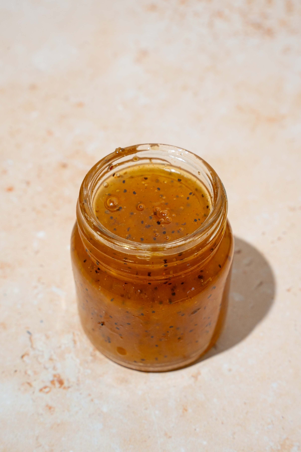 A glass jar with sweet onion sauce. The jar is on a tan counter.