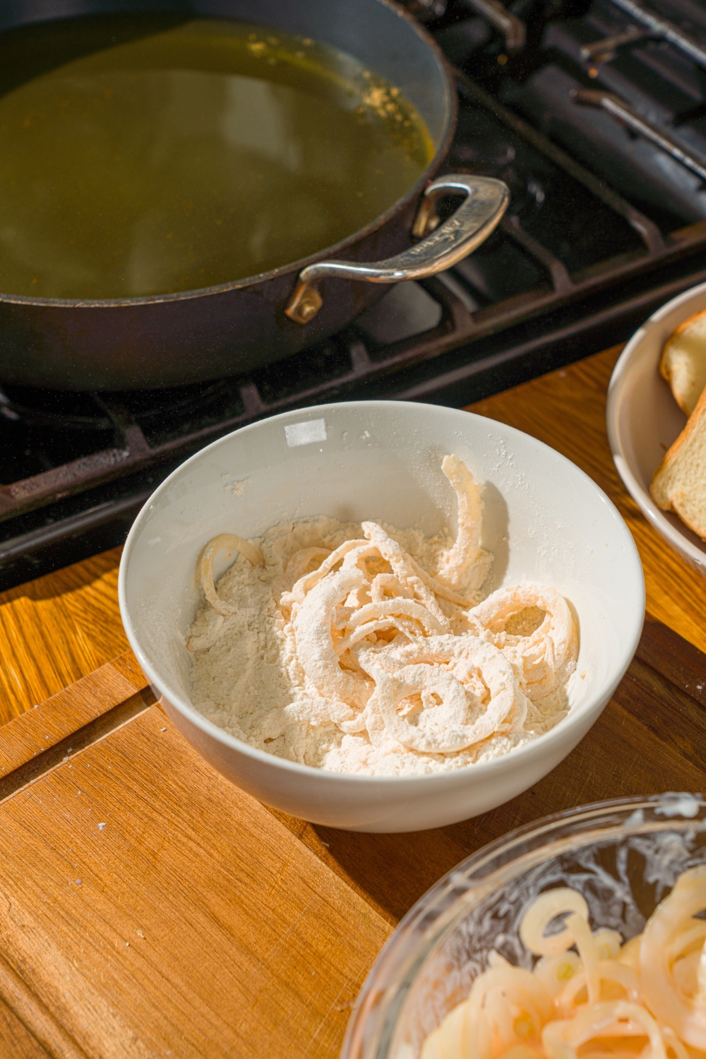 A white bowl with buttermilk soaked sliced onions dipped in a flour mixture.