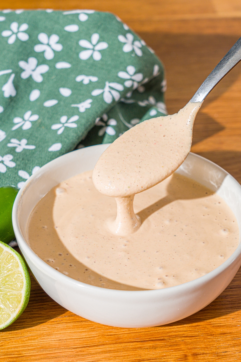 A white bowl of Taco Bell baja sauce with a spoon dipping into the bowl. The bowl is on a wooden counter with a green cloth napkin.