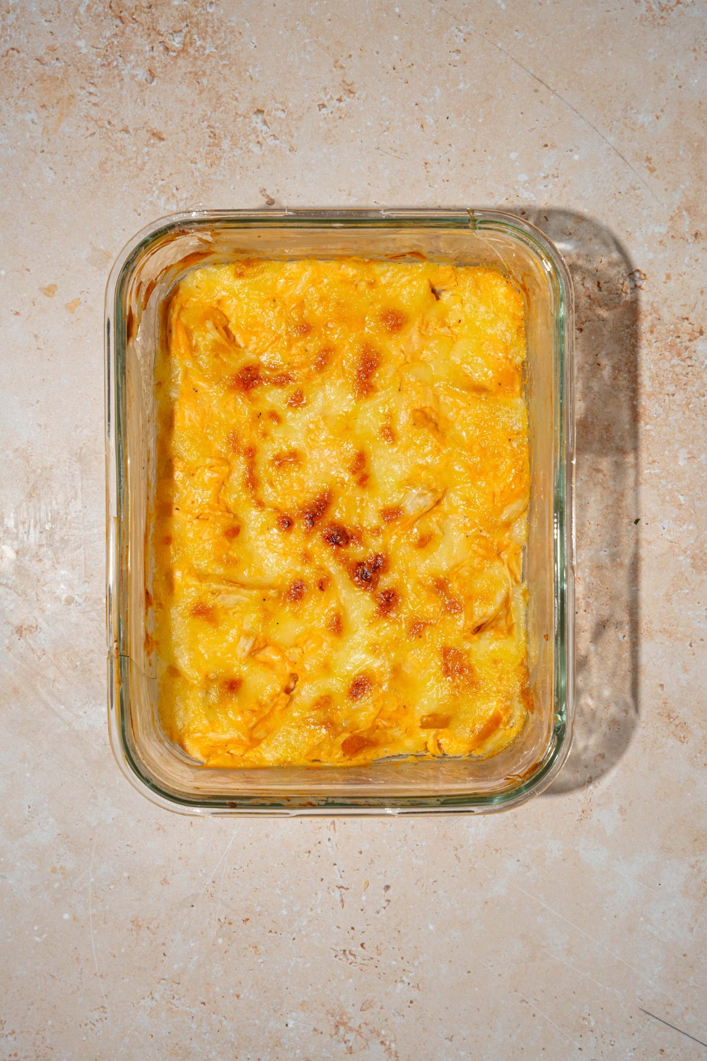 A glass baking dish with baked cottage cheese Buffalo chicken dip. The dish is on a tan counter.