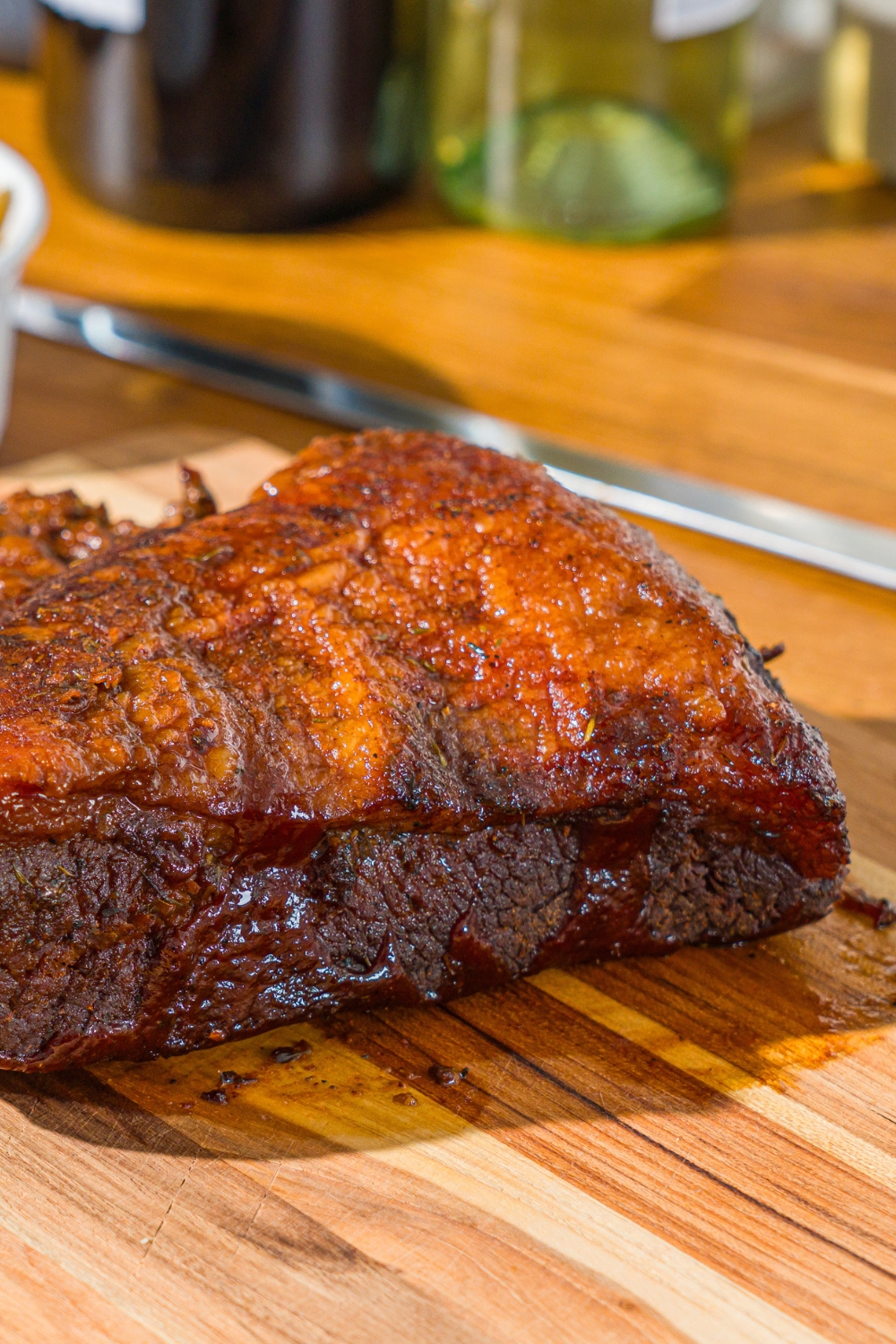 A wooden cutting board with oven baked beef brisket rubbed with seasonings and bbq sauce. The board is on a wooden counter.