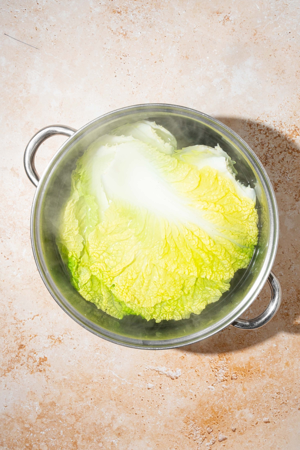 A large stock pot with cabbage leaves simmering in water. The pot is on a tan counter.