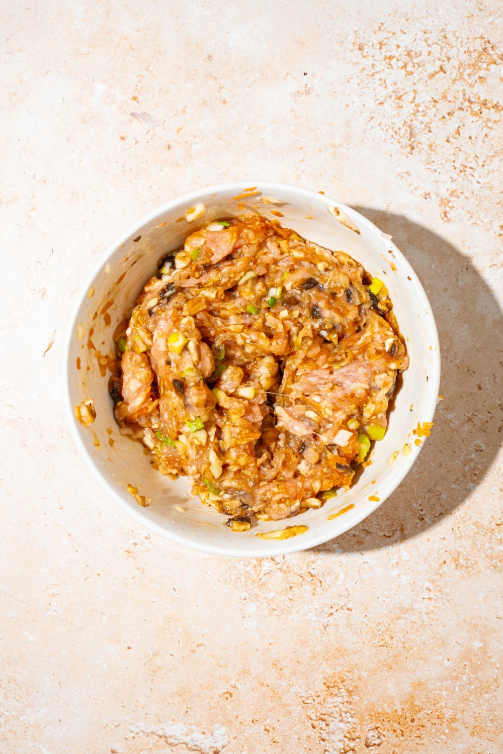 A white bowl with a cabbage dumpling mixture including ground chicken, carrots, mushrooms, garlic, ginger, and seasonings. The bowl is on a tan counter.