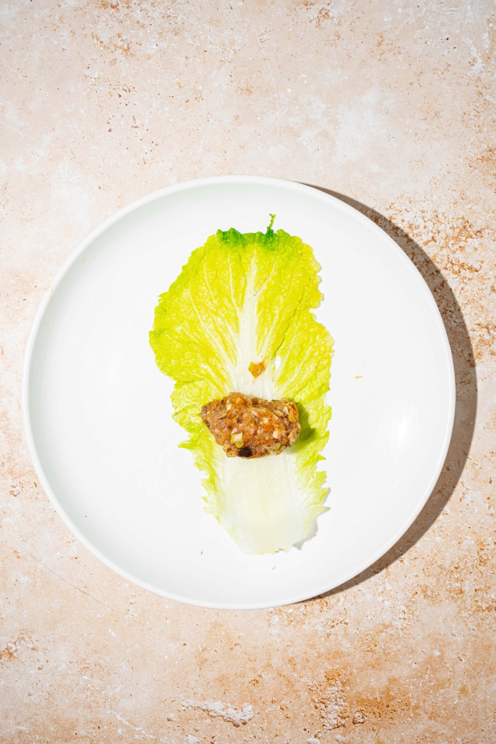 A white plate with an open cabbage leaf and small portion of a chicken mixture. The plate is on a tan counter.