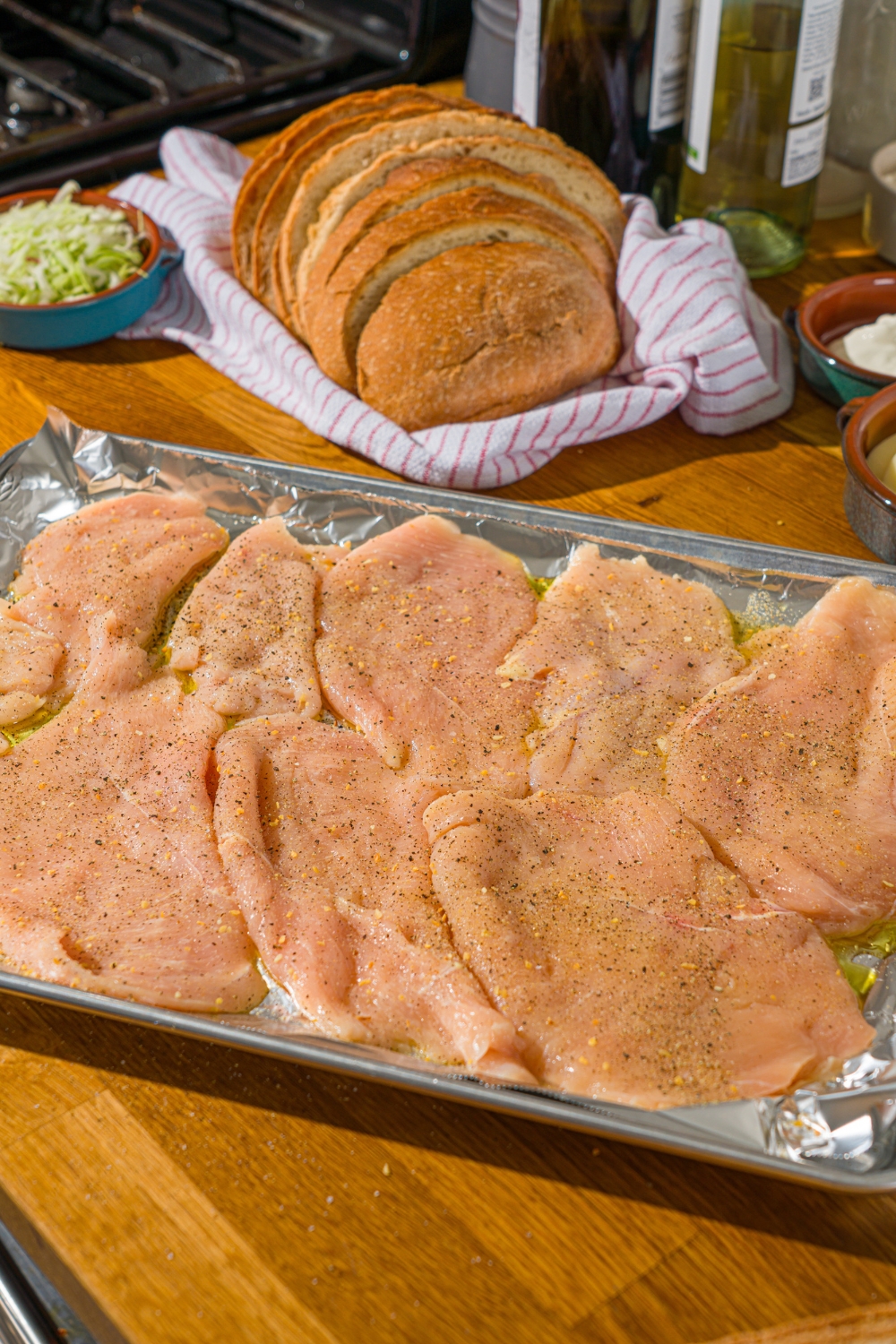 A baking sheet lined with foil with several uncooked chicken cutlets seasoned with salt, pepper, and oil.