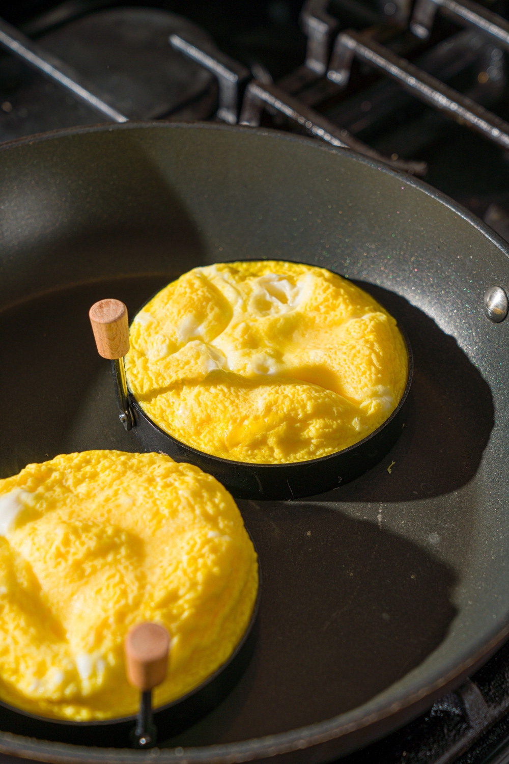 A stove with a skillet with two round molds filled with cooked egg.
