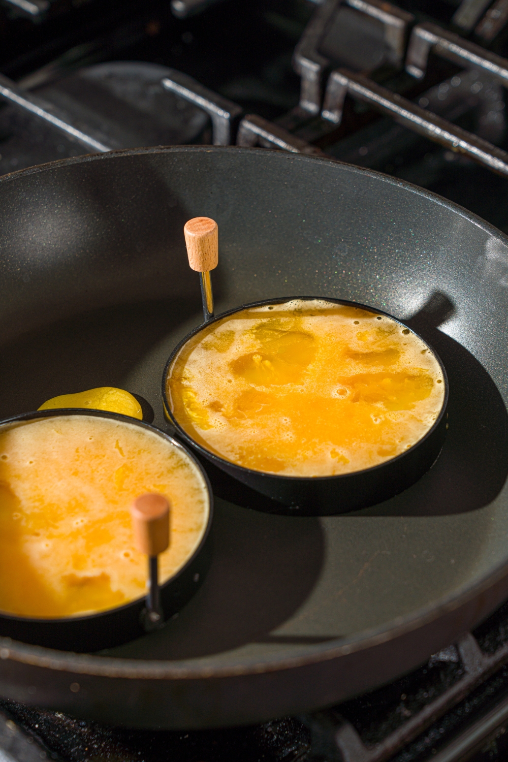A stove with a skillet with two round molds filled with whisked egg.