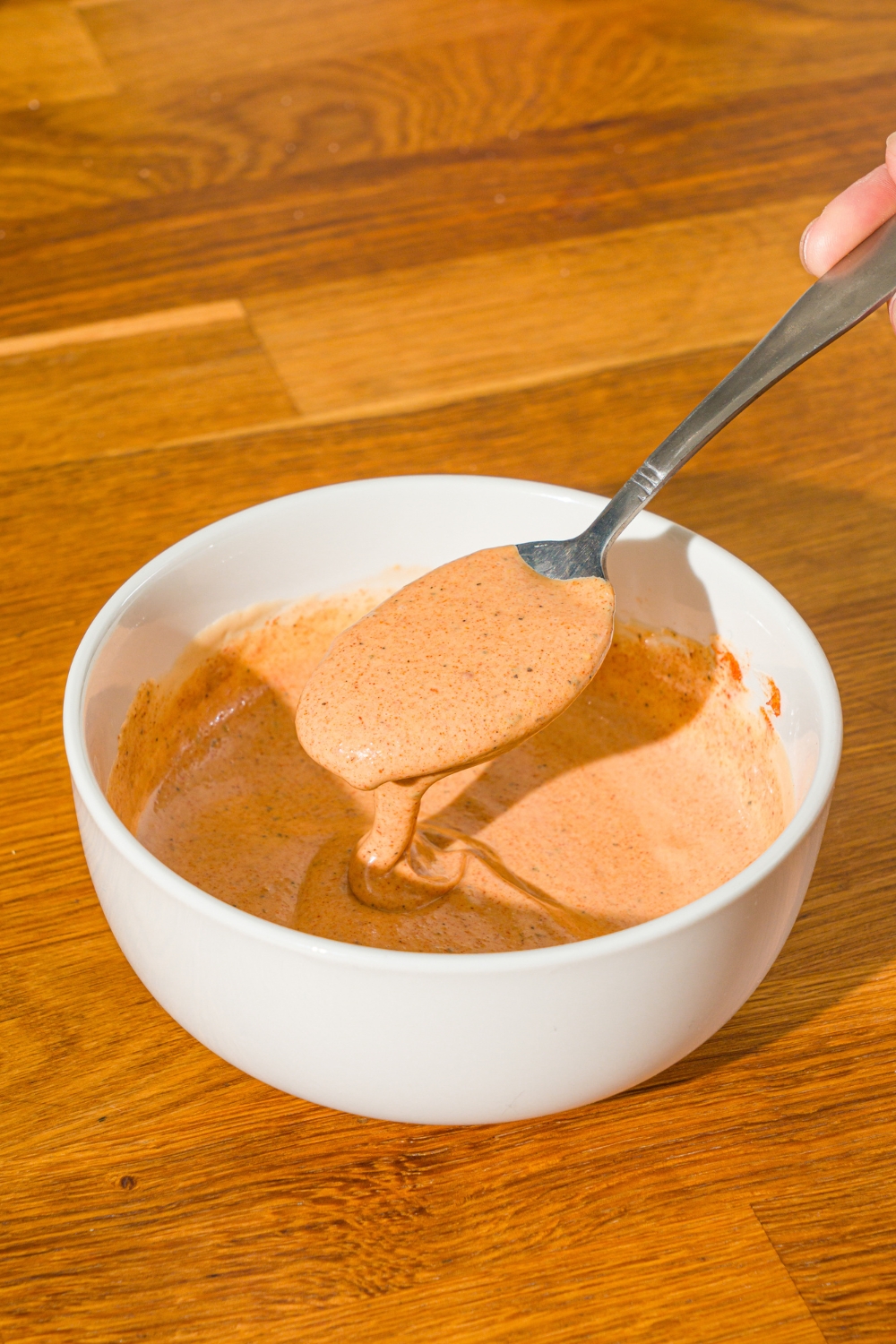 A white bowl with a spoon stirring Whataburger creamy pepper sauce. The bowl is on a wooden counter.