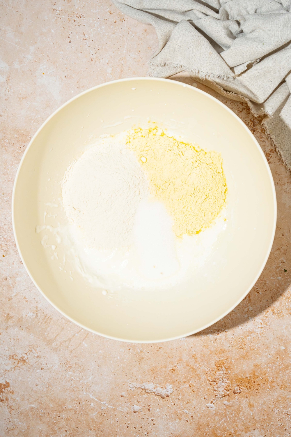 A white bowl with dry ingredients to make cornbread without eggs including flour, cornmeal, and sugar. The bowl is on a tan counter.