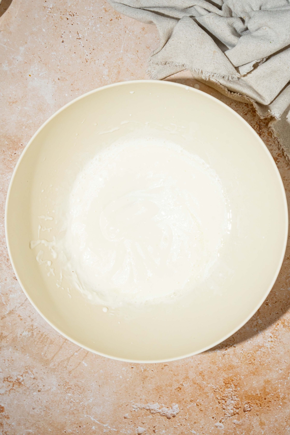 A large white bowl with wet ingredients to make cornbread without eggs including mayo, buttermilk, and oil. The bowl is on a tan counter.