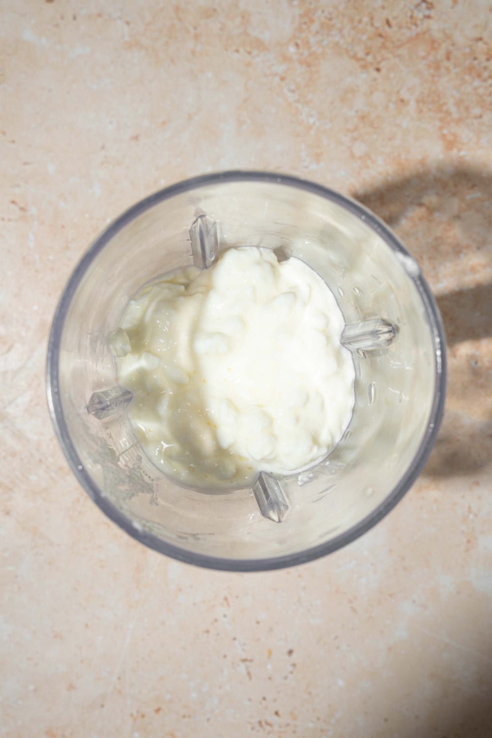 A blender with cottage cheese. The blender is on a tan counter.