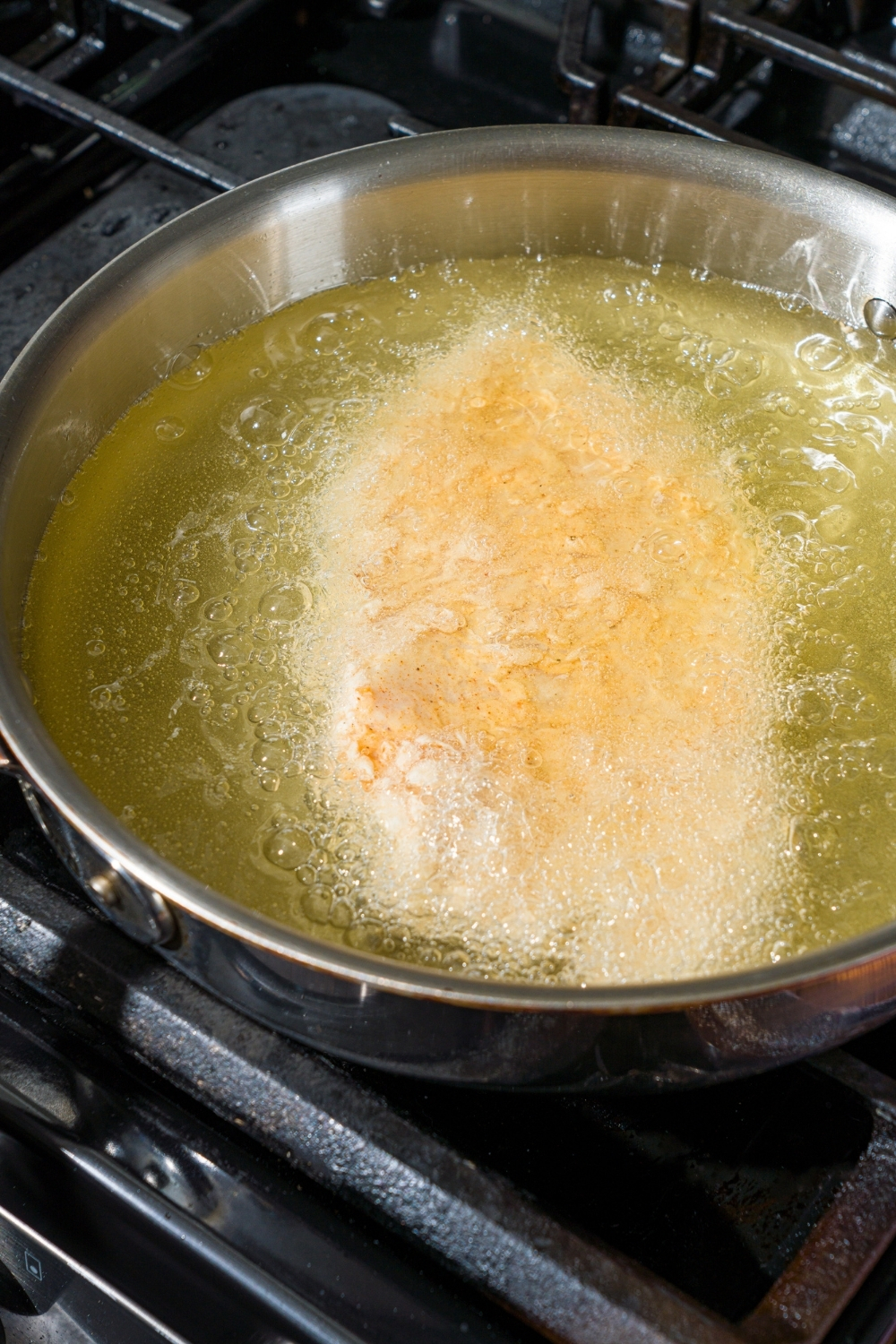 A frying pan with breaded chicken frying in oil. The pan is on a stove.