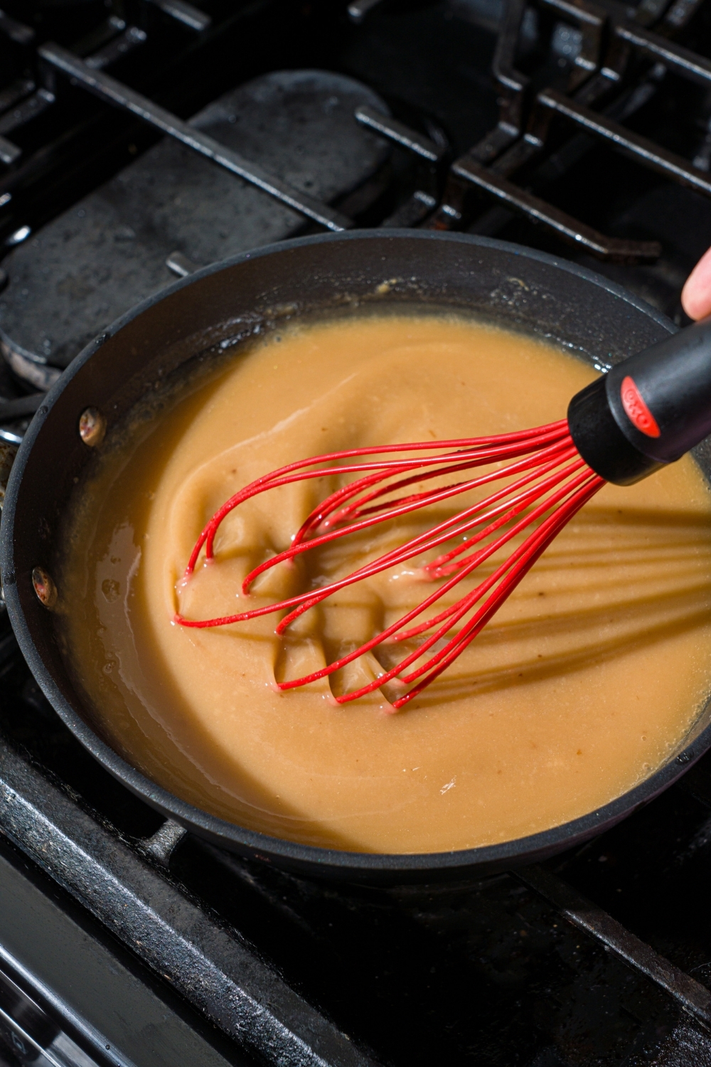 A skillet with a whisk mixing country fried chicken gravy. The skillet is on a stove.