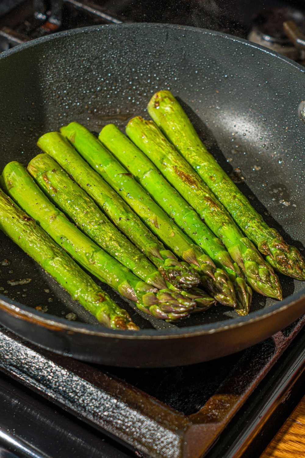 A skillet with asparagus cooking on the stove.