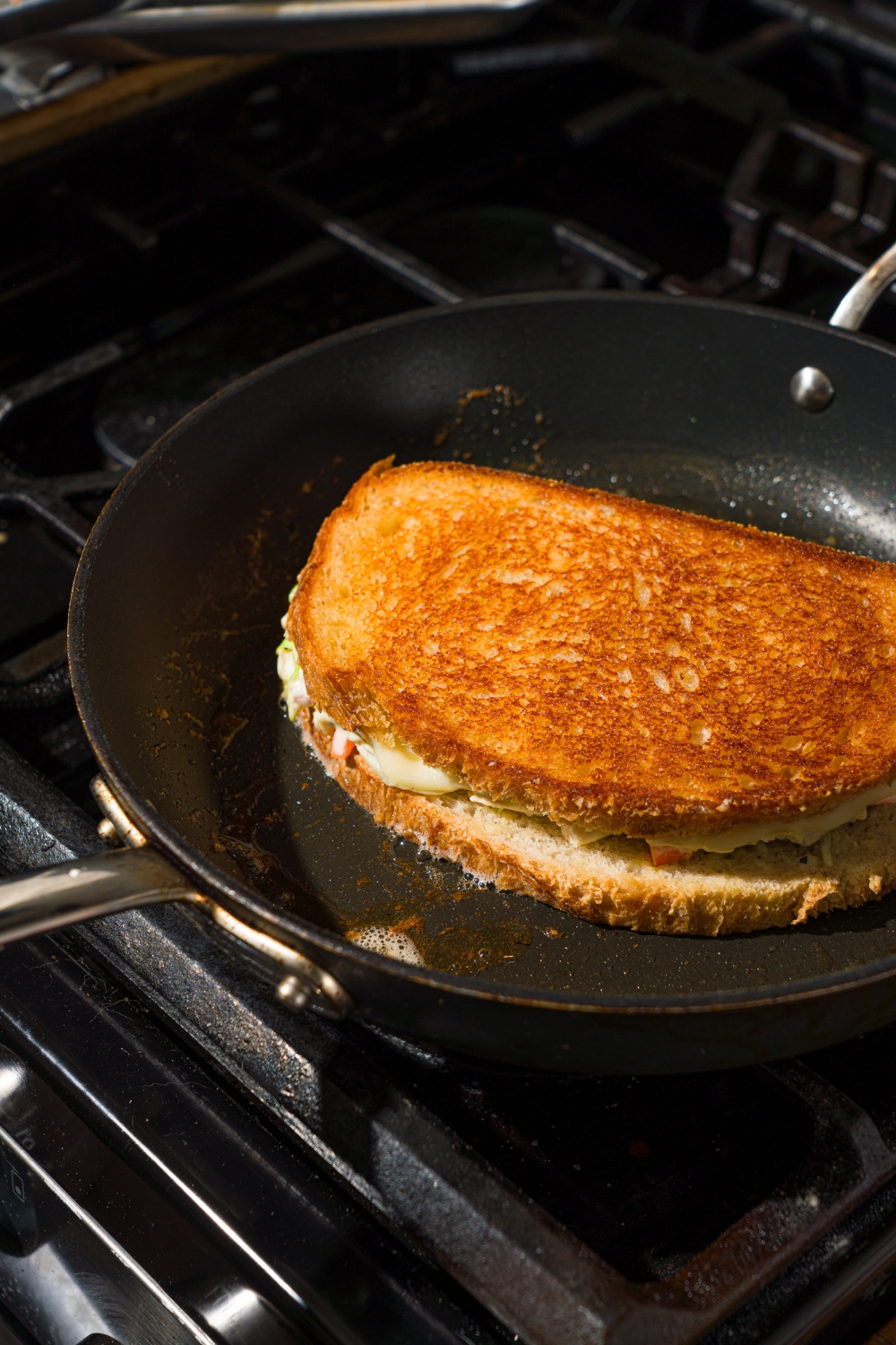A stove with a skillet cooking a chicken melt sandwich.