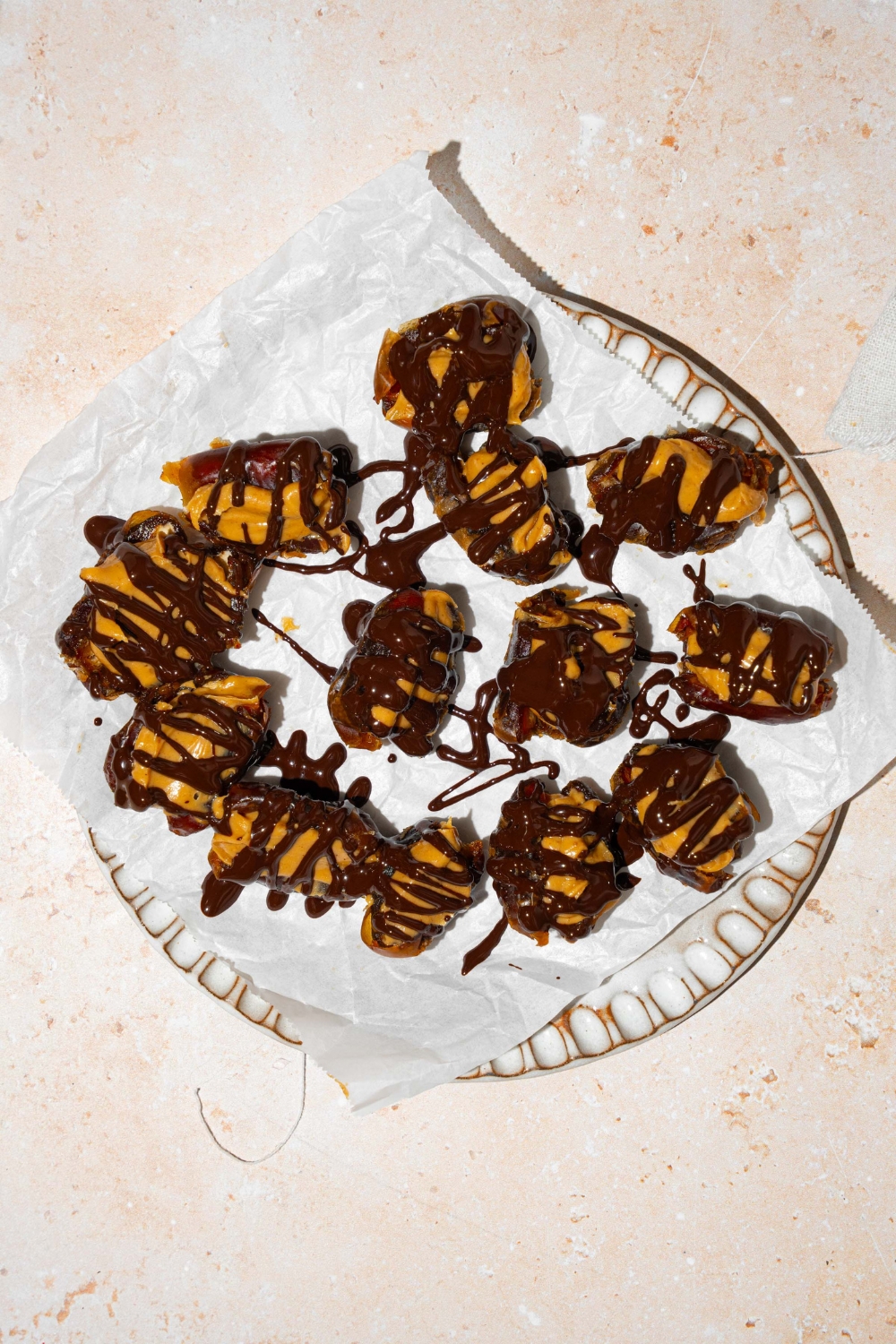 A plate lined with parchment paper with dates stuffed with peanut butter and drizzled with chocolate.