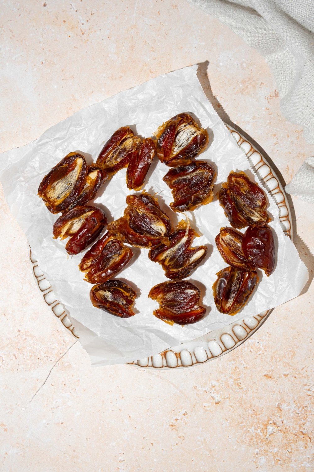 A white plate lined with parchment paper with dates sliced in half with the pits removed. The plate is on a tan counter.