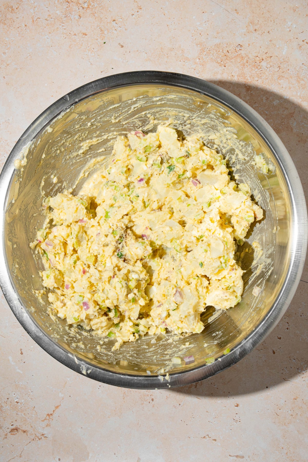 A large bowl with potato salad mixed with dressing. The bowl is on a tan counter.