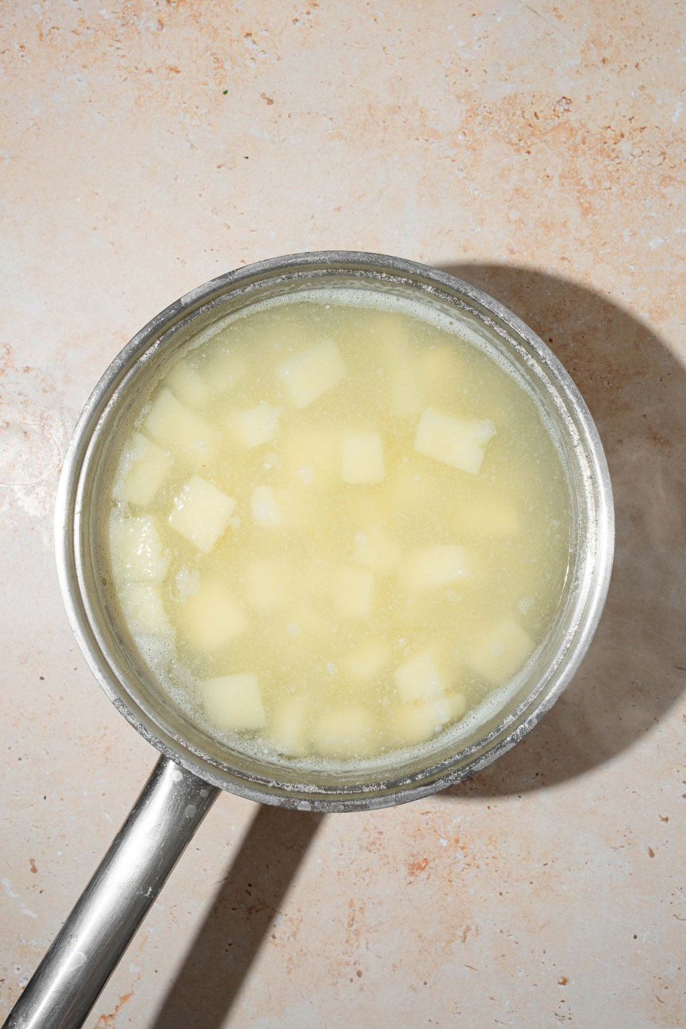 A pot with cubed potatoes cooking in water. The pot is on a tan counter.