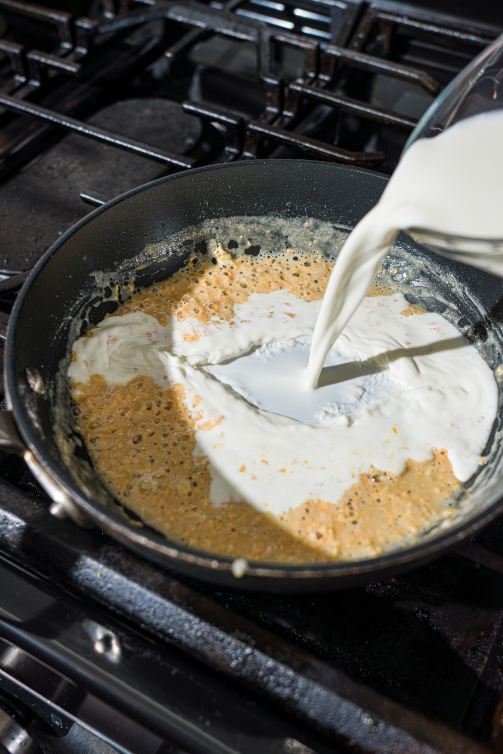 A skillet with half and half being added to a garlic roux. The skillet is on a stove.