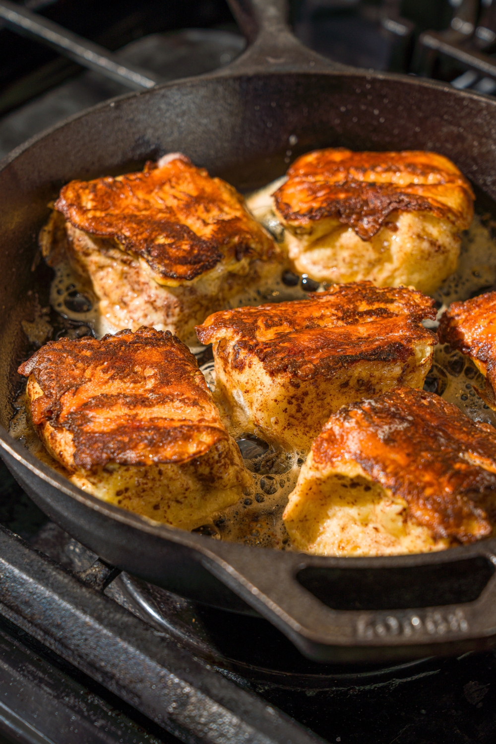 A stove with a skillet of Hawaiian roll french toast bites cooking in butter.