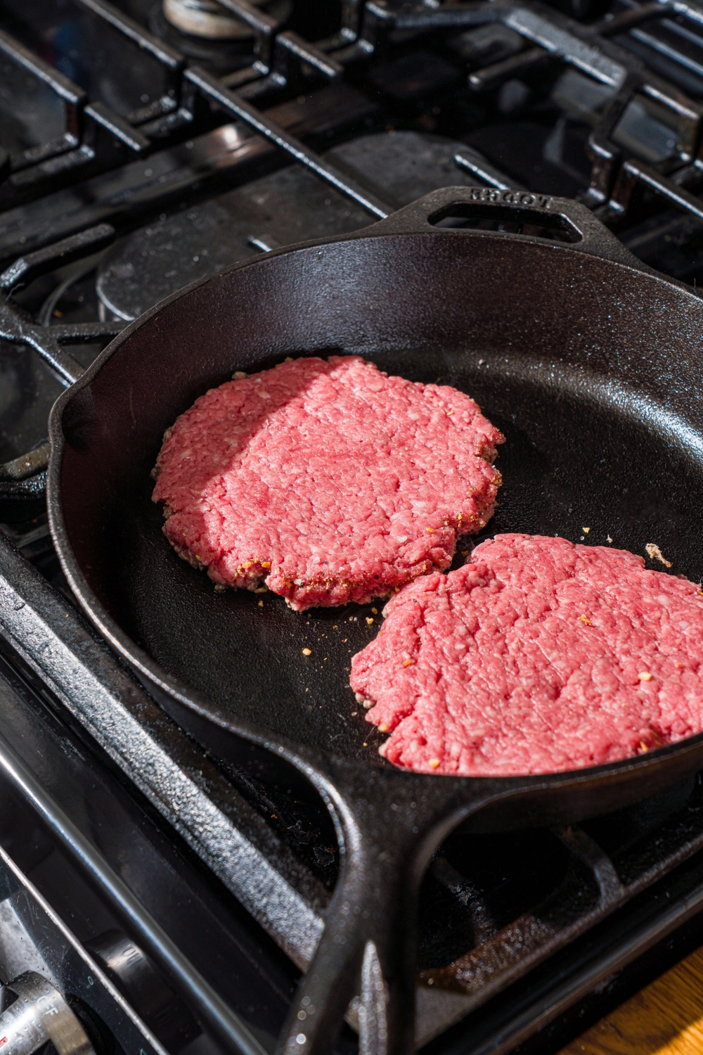 A cast iron skillet with two burger patties cooking on the stove.