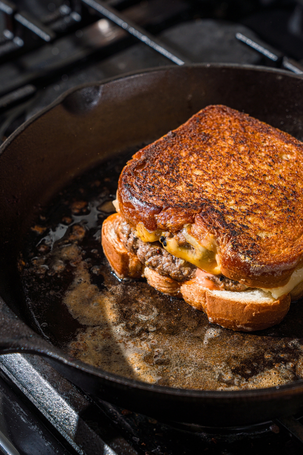 A cast iron skillet with a flipped frisco melt cooking in butter on the stove.
