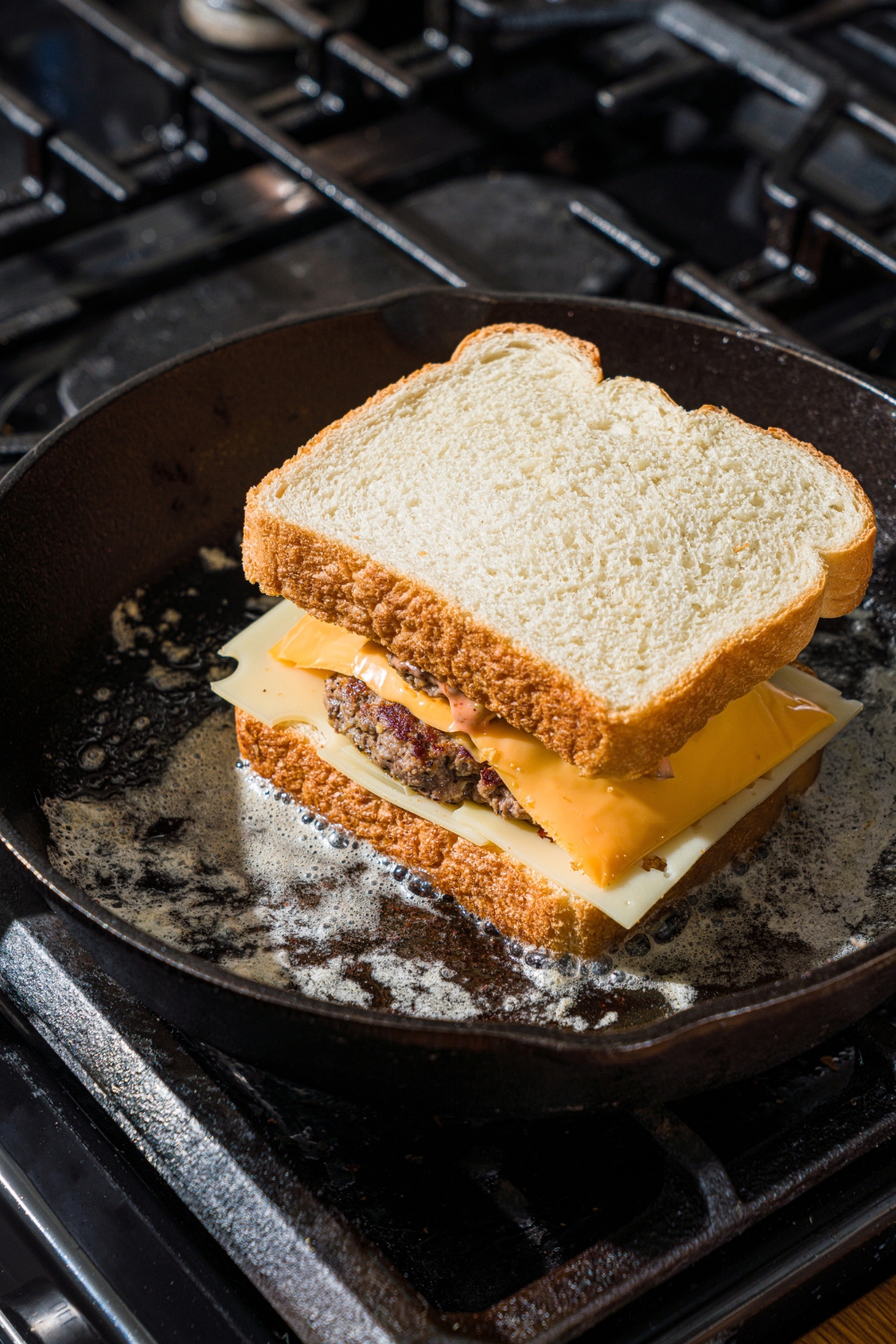 A cast iron skillet with a frisco melt cooking in butter on the stove.