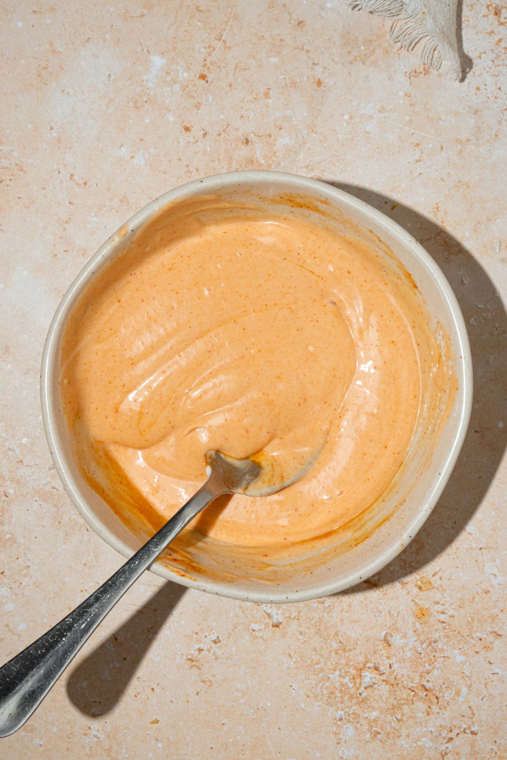 A white bowl with fry sauce. There is a spoon in the sauce. The bowl is on a tan counter.