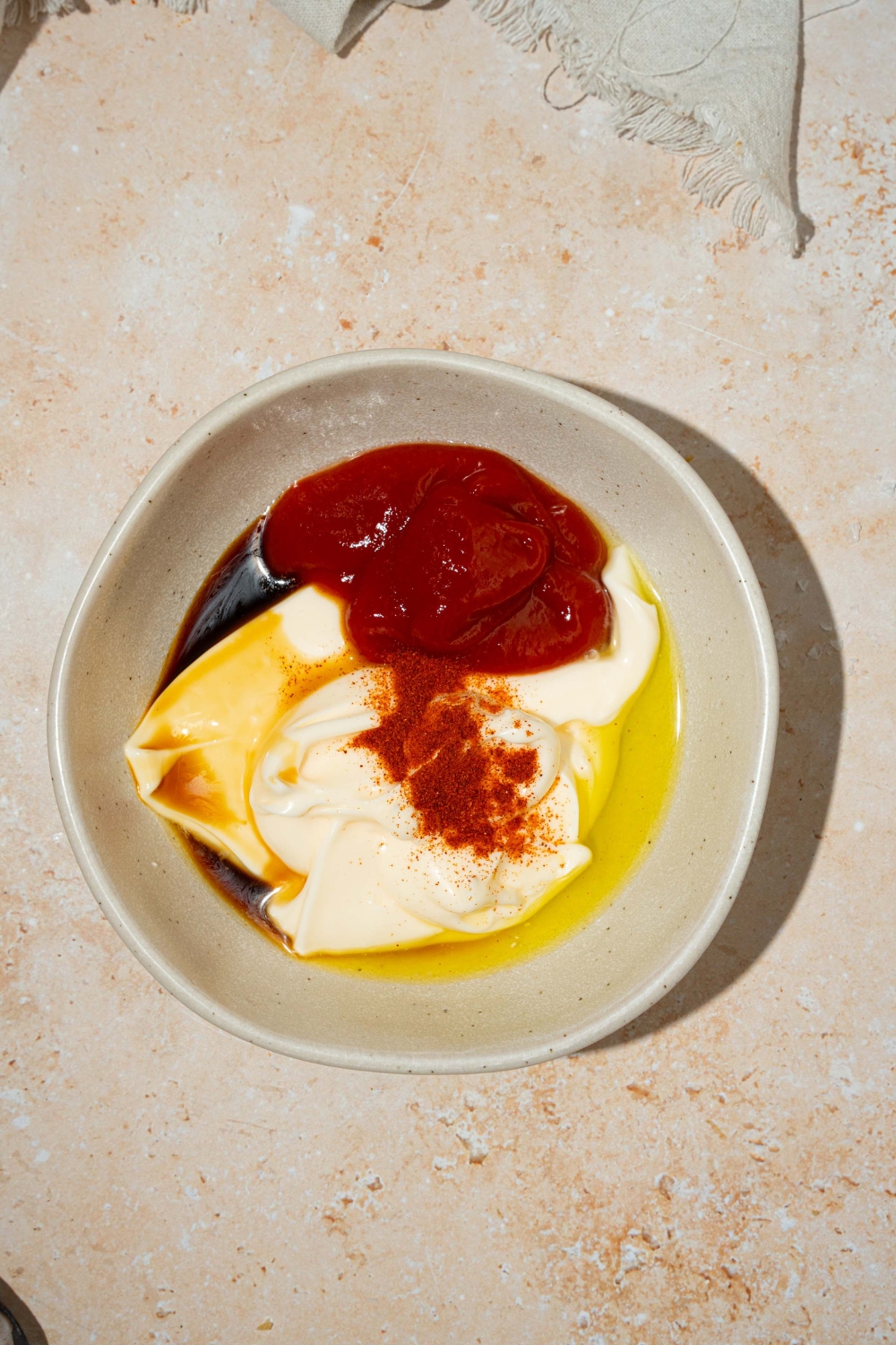 A white bowl with ingredients to make fry sauce including mayo, ketchup, Worcestershire sauce, pickle brine, and seasonings. The bowl is on a tan counter.