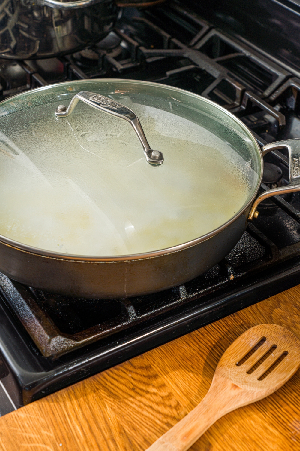 A covered skillet with a creamy garlic pasta sauce cooking on the stove.