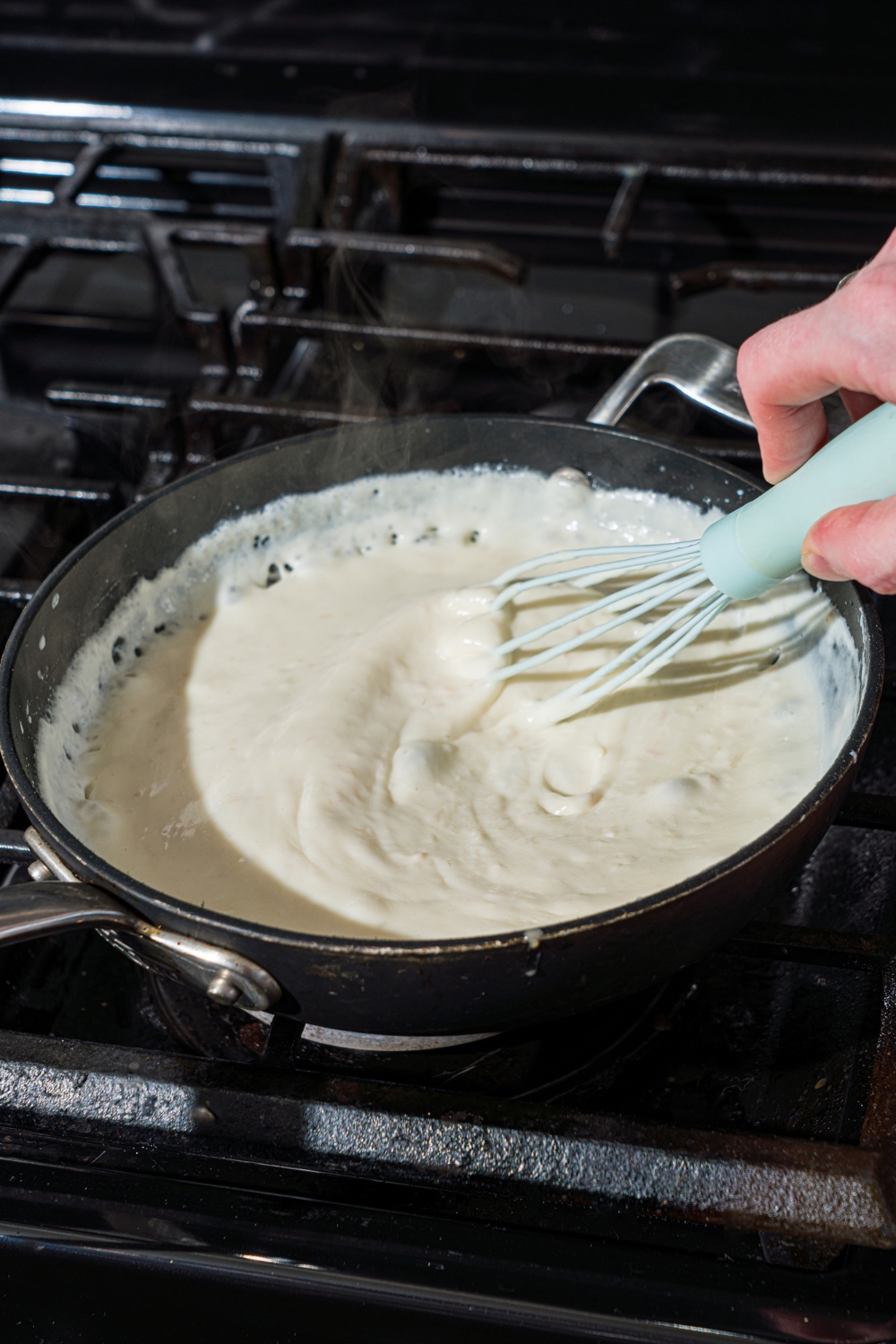 A skillet with a whisk mixing garlic white pizza sauce as it cooks on a stove.