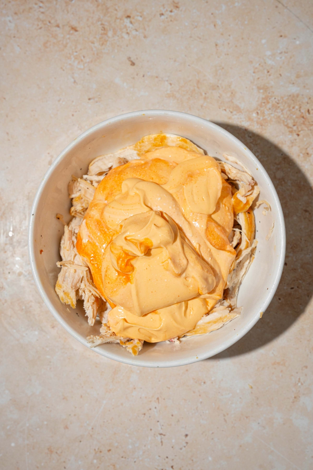 A large bowl with shredded chicken topped with cottage cheese Buffalo sauce. The bowl is on a tan counter.